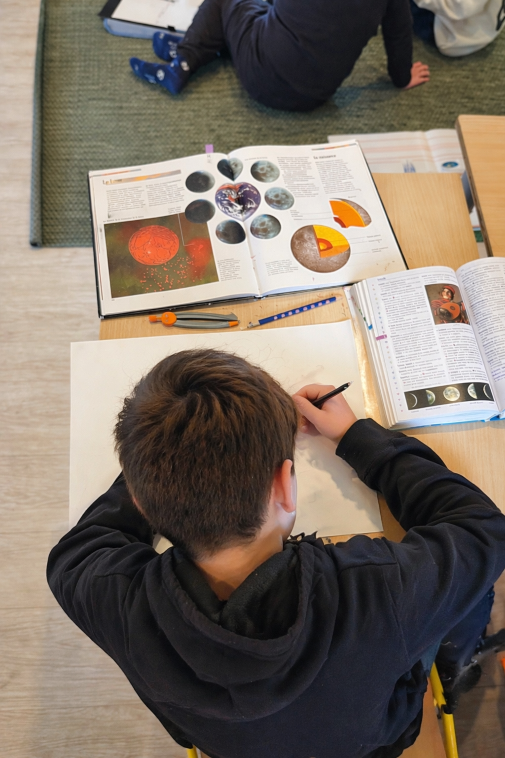 Élève en classe Montessori élémentaire engagé dans un travail autonome mêlant lecture, écriture et exploration scientifique